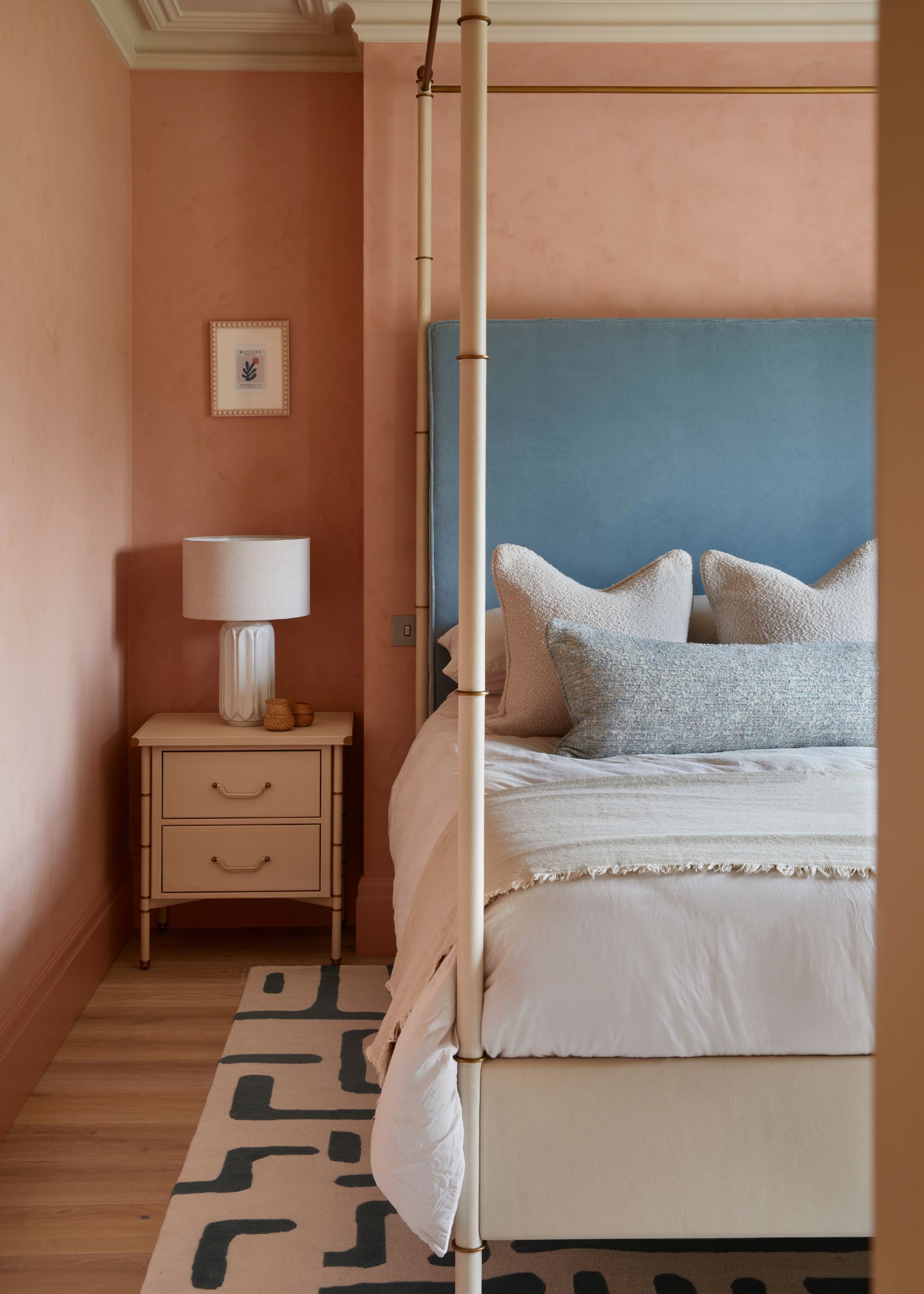 A bedroom with terracotta walls in a textured finish, a four-posted bed, a powder blue headboard, and white bedding.