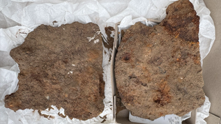 Two rust-covered fragments of metal from a Roman-era helmet. They are irregularly shaped and rust-colored.