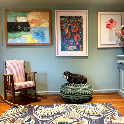 Green living room walls with framed art, behind small dog sitting on green pouffe