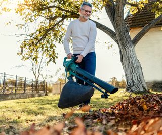 A man uses a leaf vacuum in a backyard