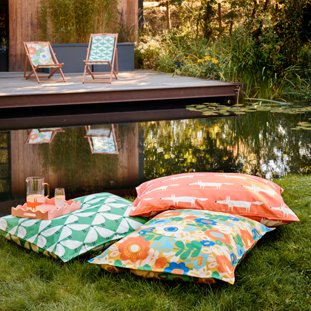 Three garden pillows on a lawn with. One has a Mr Fox print, one has a Kukkia print and the final has the Lintu print.