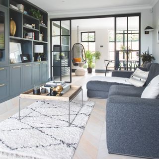open plan living room with grey storage, crittall doors through to dining room, coffee table, hanging chair in dining room space, grey sofa