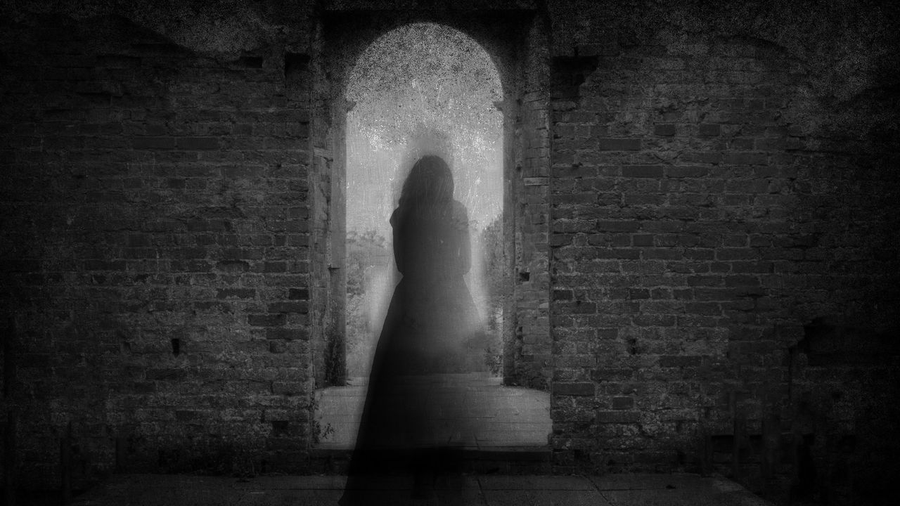 Black and white photo of a phantom standing in the doorway of an abandoned house.