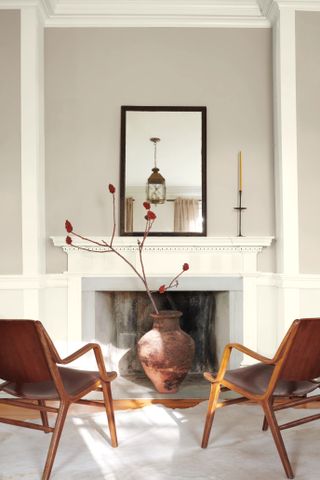 A living room with a fireplace, two mid-century style chairs, and walls painted in a delicate taupe shade