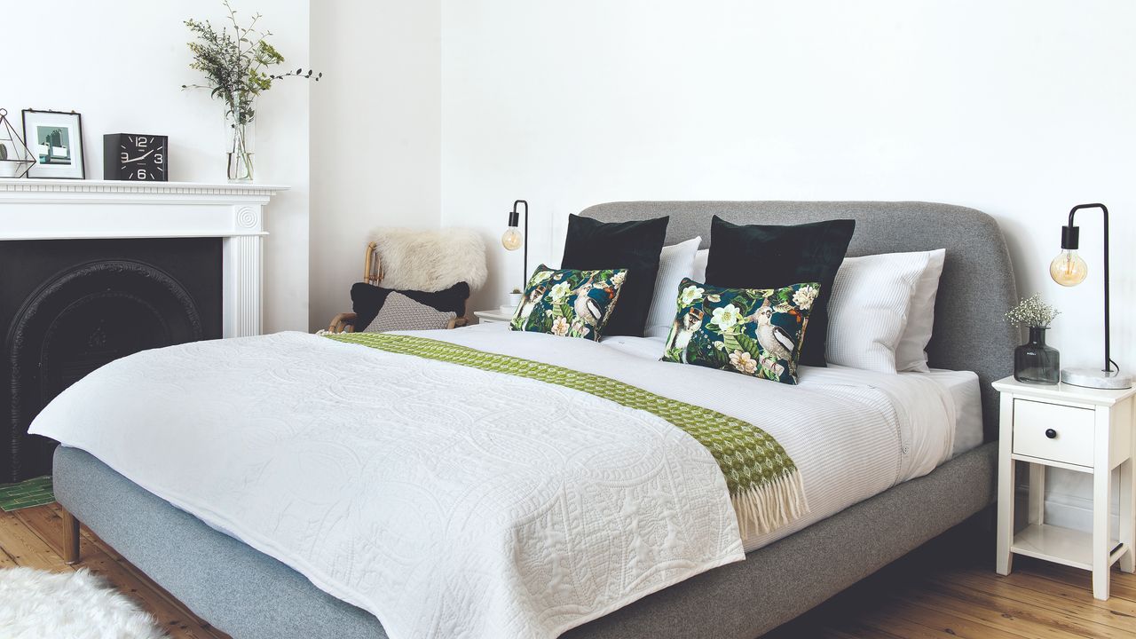 Grey king size bed with white bedding and patterned cushions with bedside table