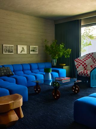 Living room with limewashed green-beige walls, electric blue sofa, white and red checked armchair and coffee table with button legs