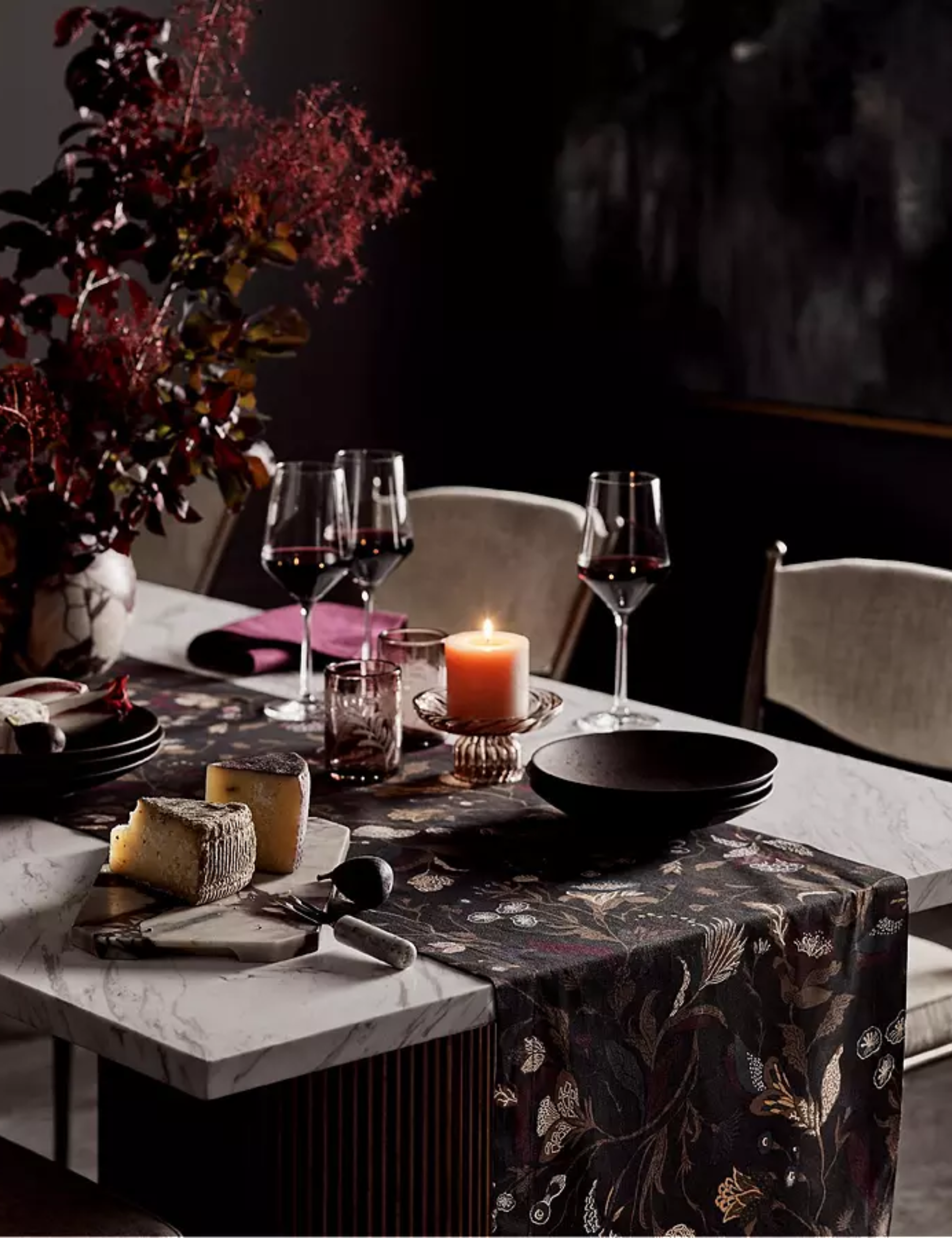 Moody fall setting featuring an oxblood floral arrangement, damask table runner, wine glasses, and a darkly tinted water tumbler.