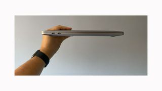 Image shows a hand holding a closed MacBook Pro M1 from the side.