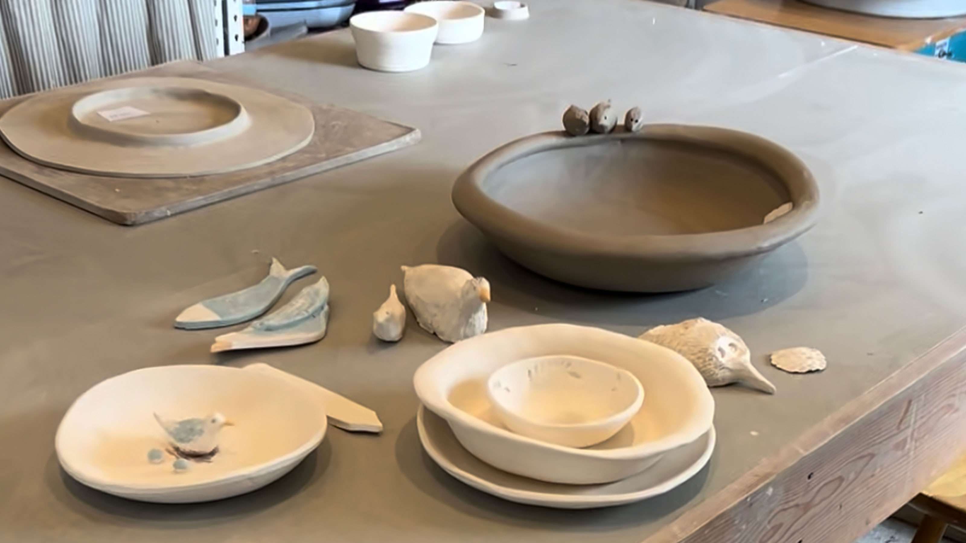 Table covered in clay bowls and pottery mid-way through being made 