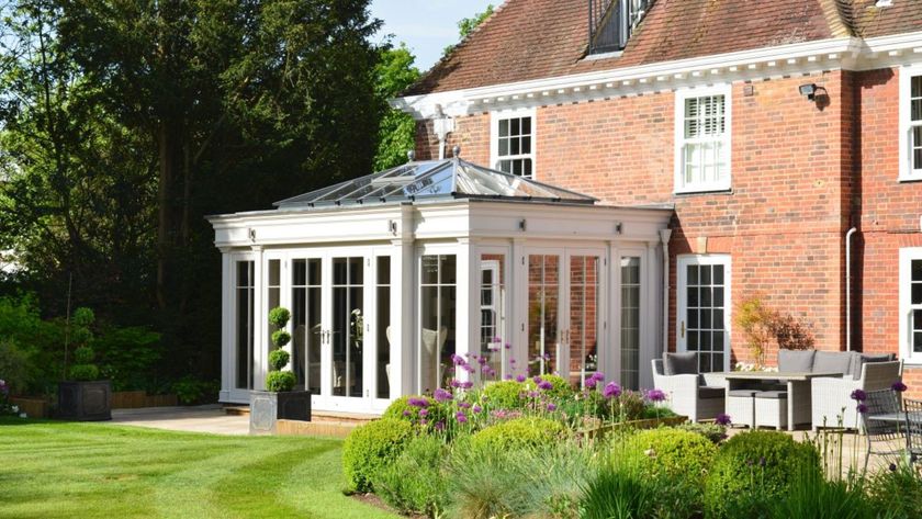 A classic white framed conservatory with a glazed roof adjoined to a redbrick Georgian house