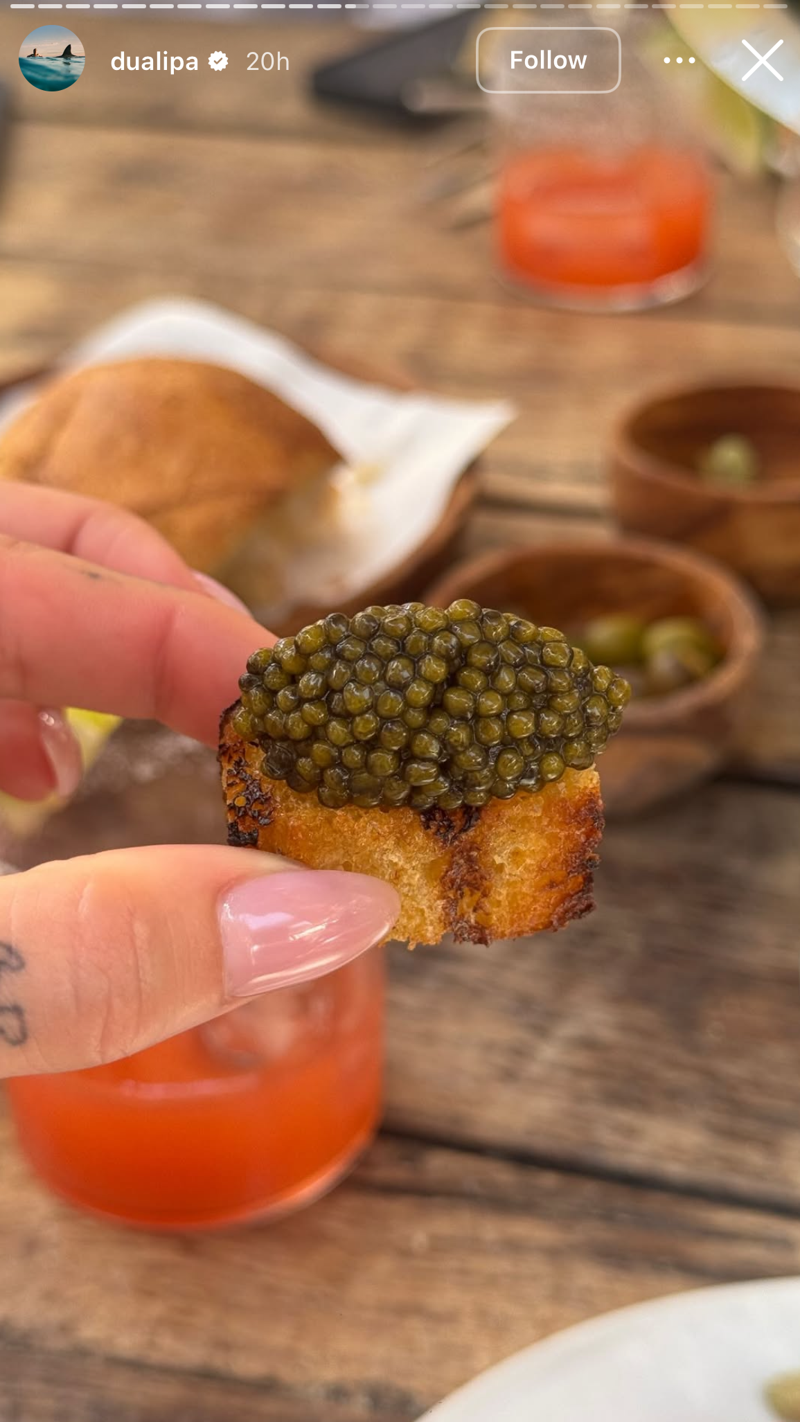a person with neutral nails holding a piece of bread topped with caviar