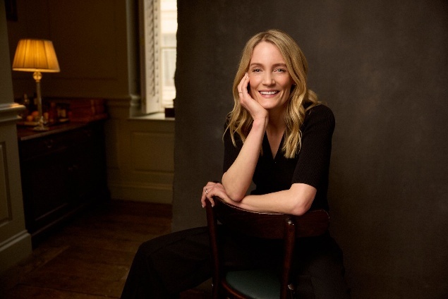 author lucy foley smiles and rests her chin in her hand while sitting in a chair as she poses for a headshot