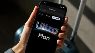 The Saily Ultra Plan on a phone held by a man, a travel suitcase is visible in the background