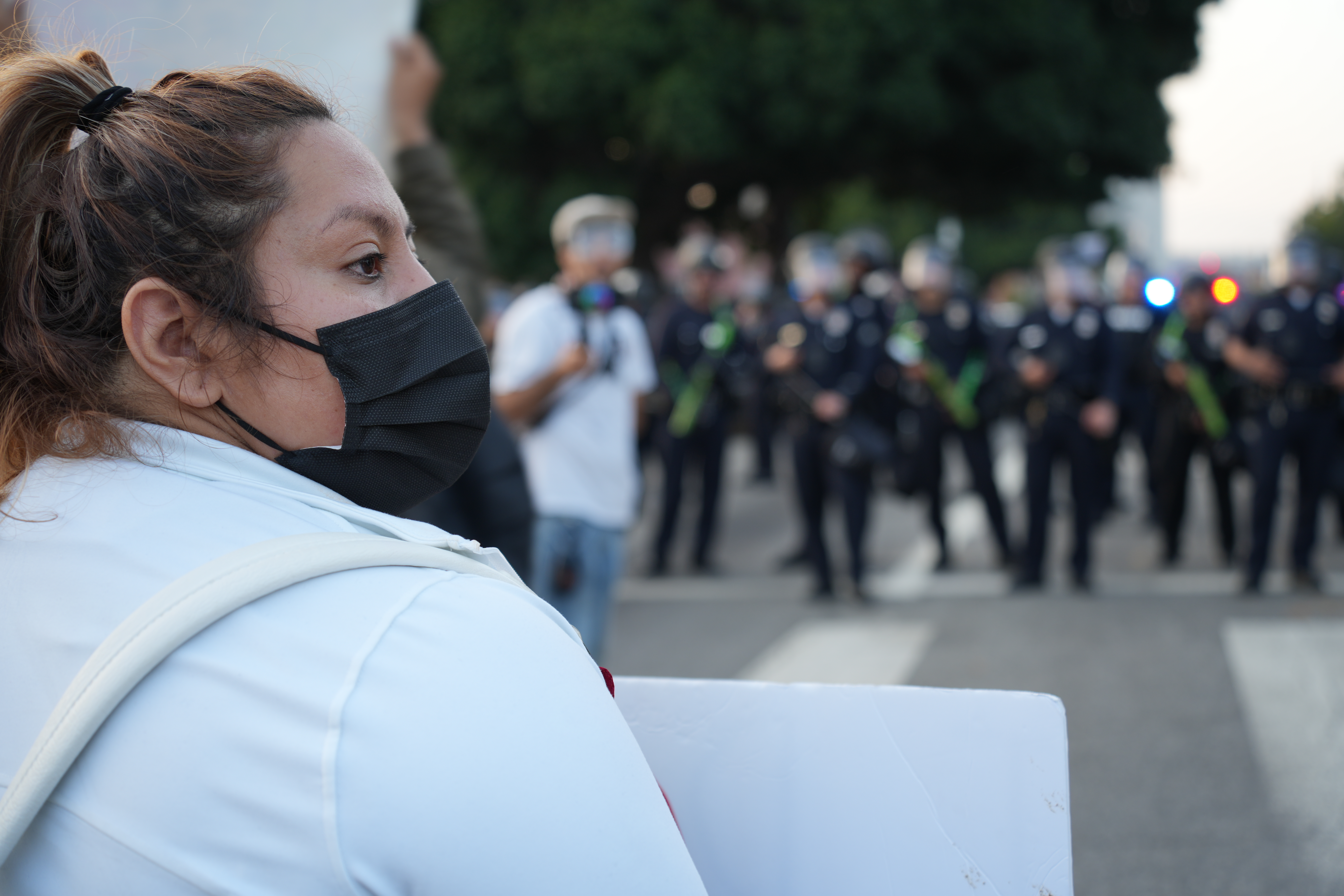 A masked protester faces a line of police officers on a downtown street.