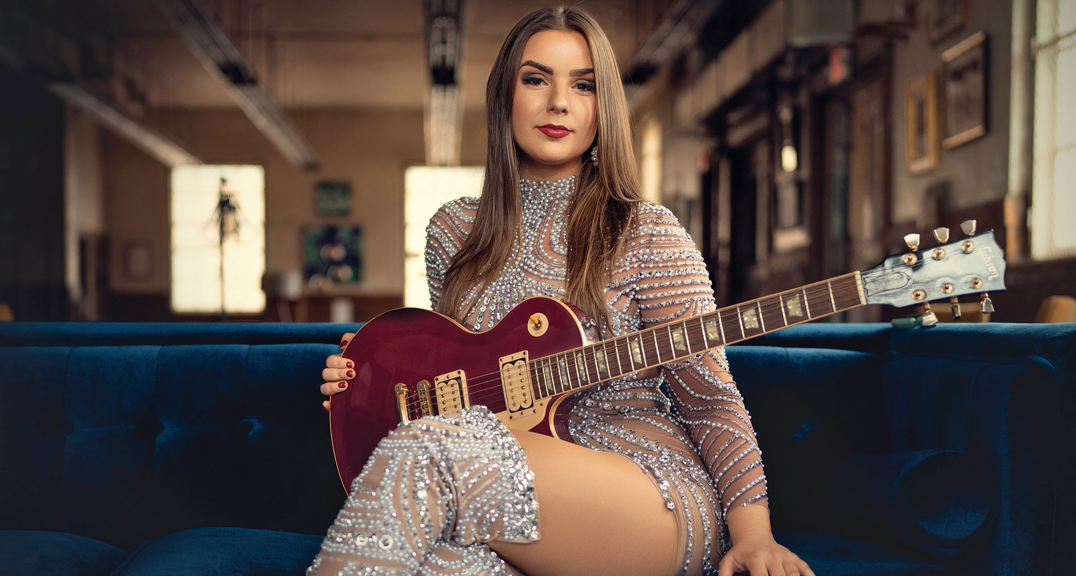 Ally Venable sits on a couch with her Magenta colored Les Paul