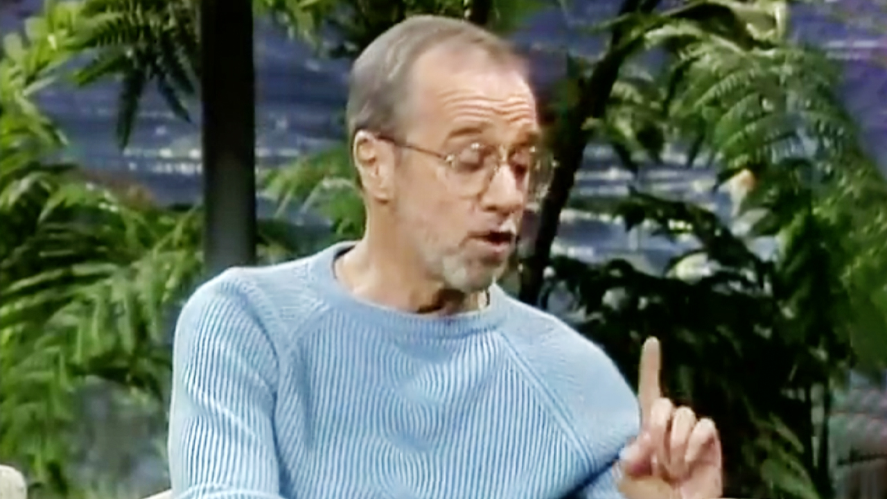 George Carlin, wearing glasses and a stripped blue shirt, making a great point while appearing on The Tonight Show Starring Johnny Carson.