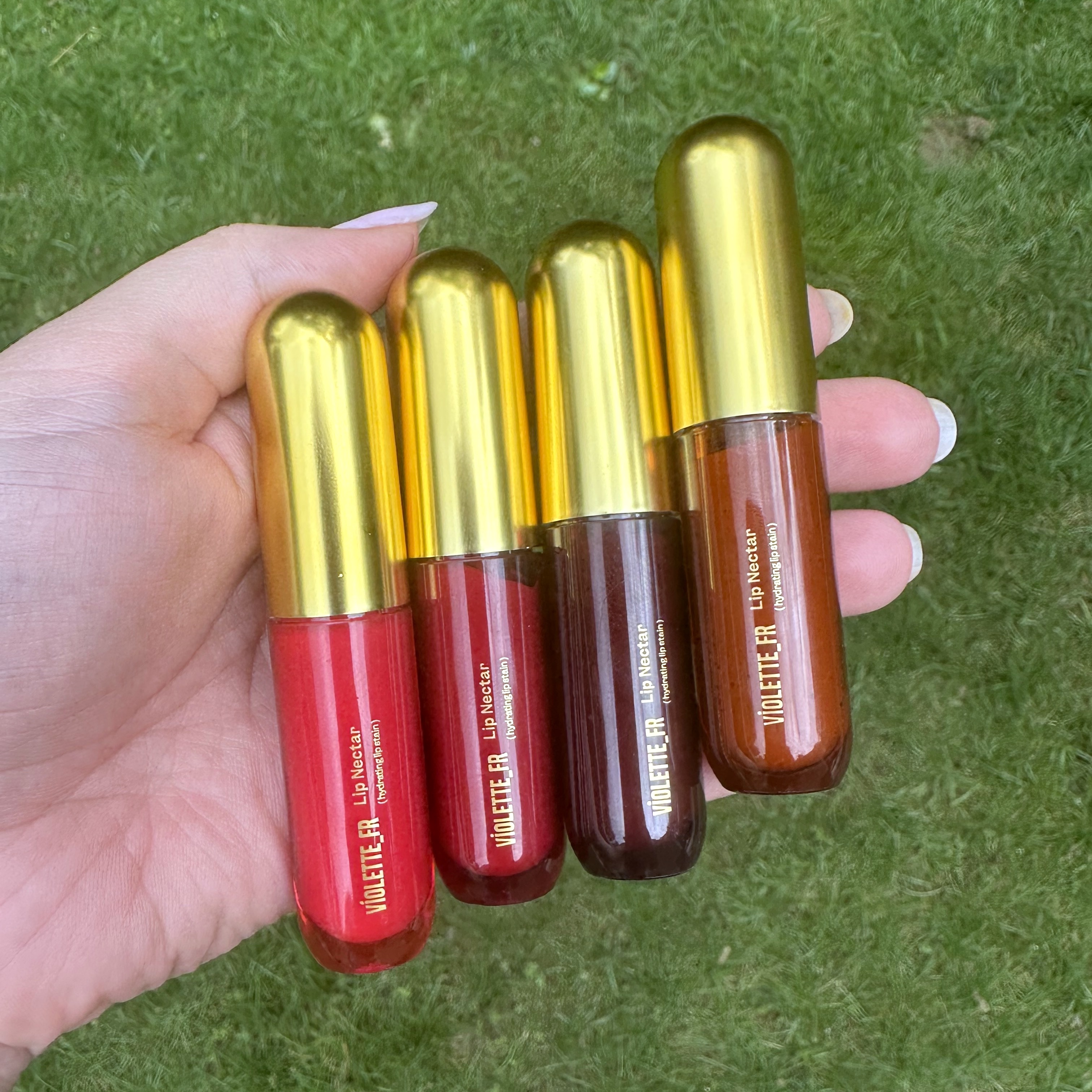 Person holding Violette_FR Lip Nectars in four different colors.