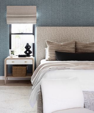 drapes vs blinds, blue and cream bedroom with blue textured wallpaper, neutral patterned upholstered headboard,, rug, linen blind, side table