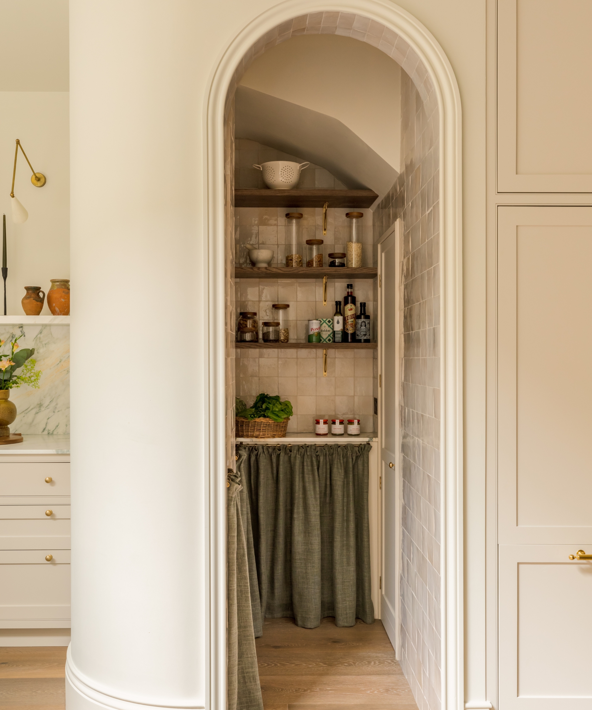 A small pantry under the stairs with an arched doorway and skirted cabinets