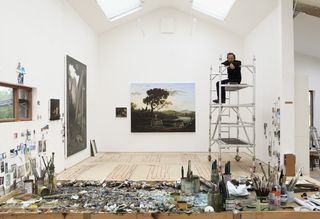Ged Quinn seated atop the scaffolding he uses for his larger paintings in his studio in Penzance, Cornwall