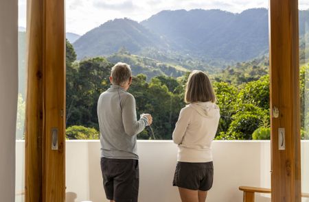 An older couple is enjoying a cup of coffee on their hotel deck overlooking the mountains in Costa Rica.