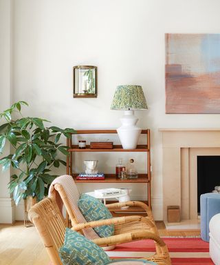 living room with fireplace, painting, red striped rug, mid century bookshelf and green patterned cushions on rattan chairs