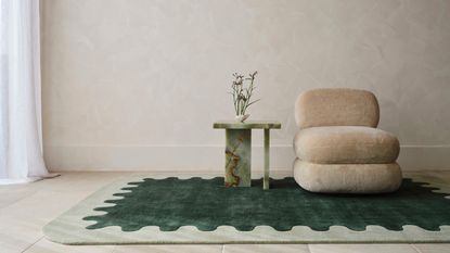 Image of a living room from a low vantage point. There is a wavy sage and forest green area rug with a beige boucle armless chair and a green marble side table. 