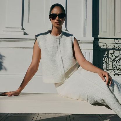 Woman wearing cream outfit and dark sunglasses sat on step