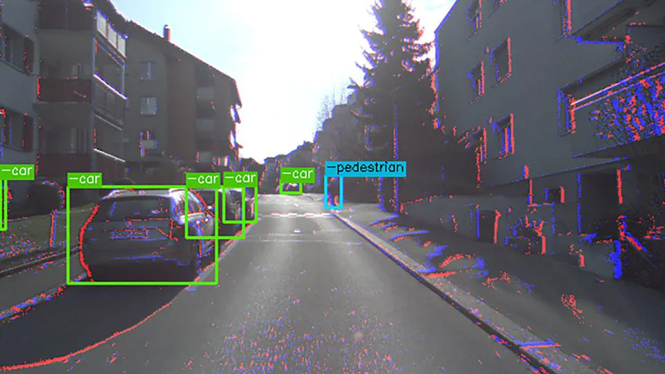 Image shows colour information from the colour camera and events (blue and red dots) from the event camera; bounding boxes show the detection of cars by the algorithm