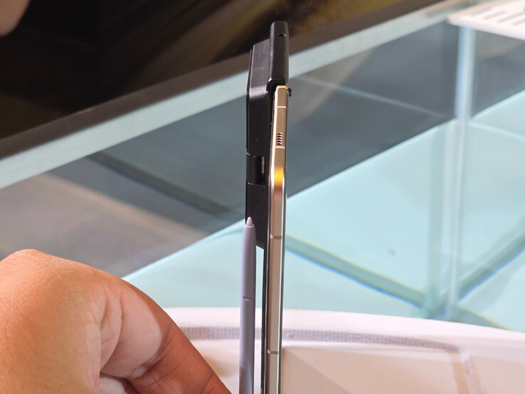 The Honor Magic V5 is held next to a Samsung S Pen to highlight its slim profile.