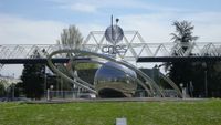 A metal ball surrounded by metal rings sits on a grassy lawn in front of a glass building with the letters CNES on the front