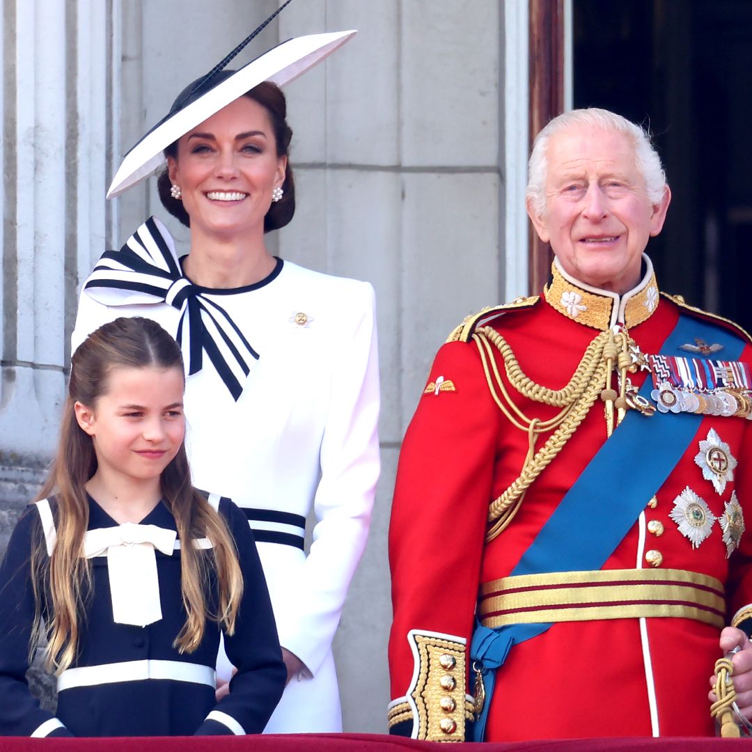 Kate Middleton wears a white dress with navy accents and a matching hat while King Charles wears red military uniform
