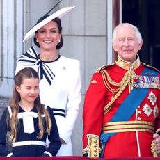Kate Middleton wears a white dress with navy accents and a matching hat while King Charles wears red military uniform