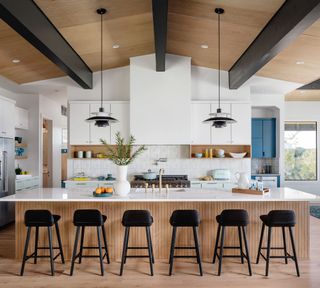 Scandi, mono kitchen with wood floor, and matching wood panels on island and vaulted ceiling, with dark contrast beams and bar stools