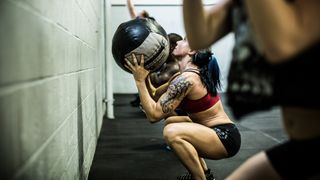Woman squats holding large medicine ball midway through wall ball exercise