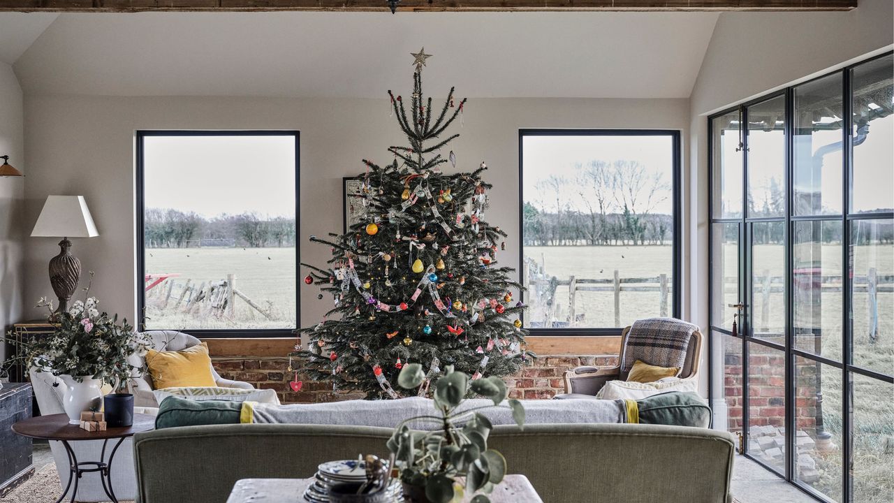 Large decorated Christmas tree between windows framed by seating area in living room