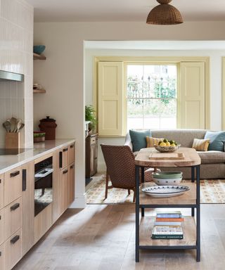 kitchen with wooden cabinetry and pale tiles and a freestanding wooden island with a living space in background and yellow shutters