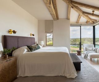 wooden beamed bedroom with wrap around windows and a large bed