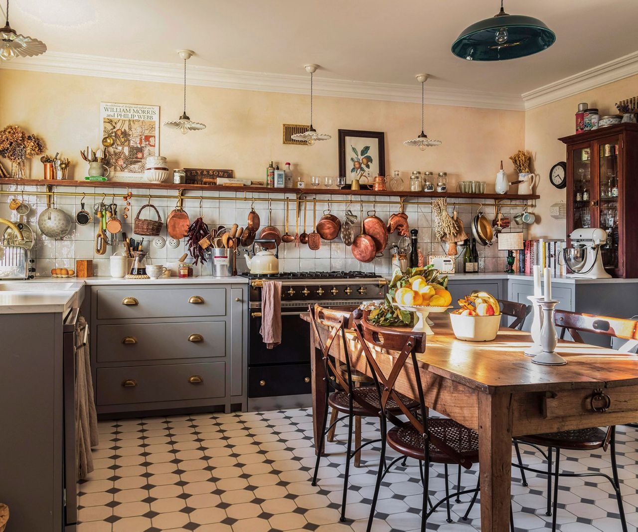 A French country style kitchen with gray cabinets, white wall tiles, and a brass pot hanger
