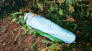 Person sleeping in sleeping bag under natural shelter, in woodland