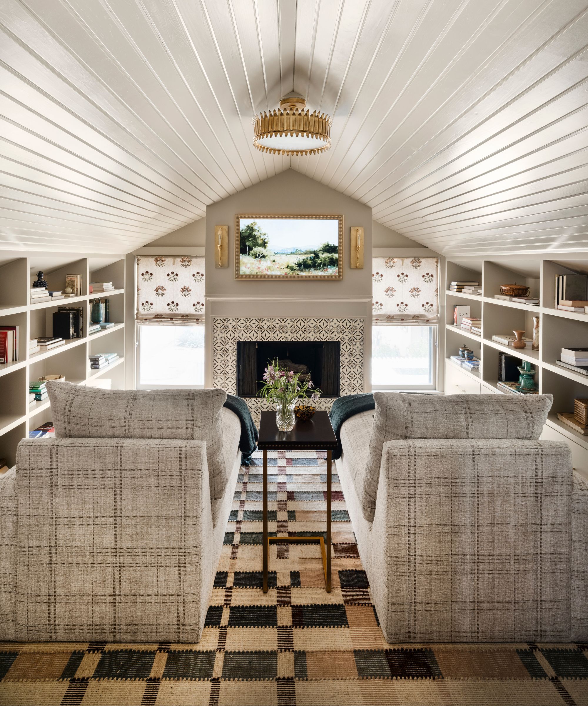 a snug room off of a primary bedroom with sloped paneled ceiling, a fireplace, walls lined with bookcases and two plaid loungers