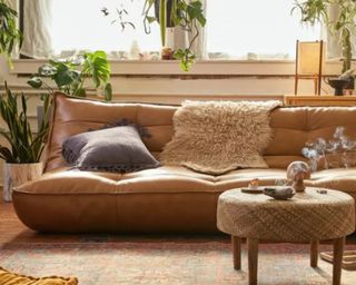 A brown leather-style sleeper sofa in a living room with pot plants, a coffee table, a throws.
