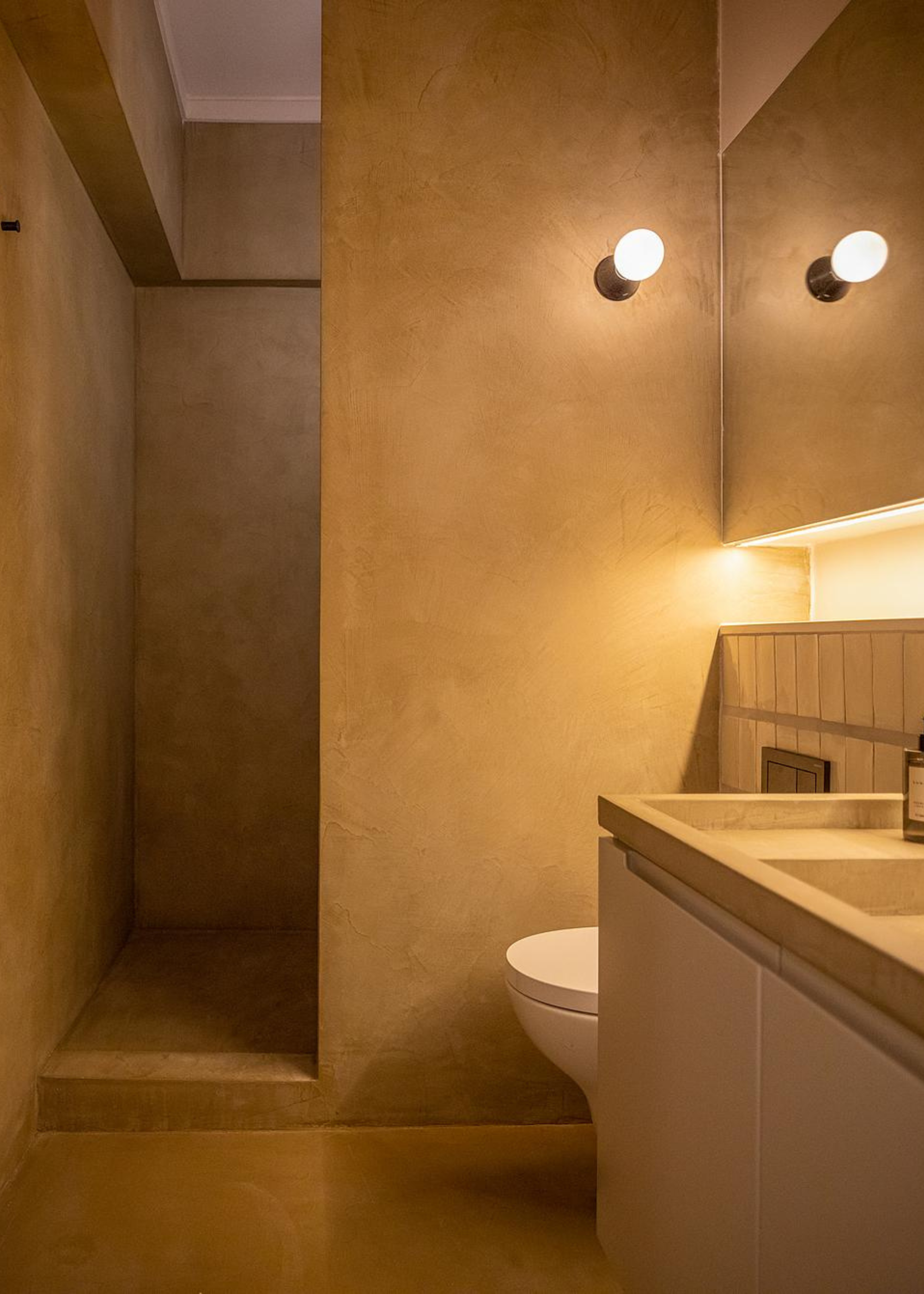 A microcement bathroom with a sink and toilet in the corner of the room