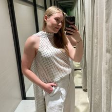 Woman wears polka dot top and white linen trousers