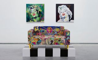 Two paintings of Merylin Monro are hung on the wall. Below them is a colorful sofa.