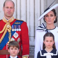 Prince William wears red military uniform and Kate Middleton wears a white dress with navy detailing, as they stand on the Buckingham Palace with their three kids, Prince George, Prince Louis, and Princess Charlotte