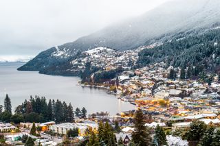 Houses are lit up at dusk against the snow-covered trees in Queenstown, New Zealand