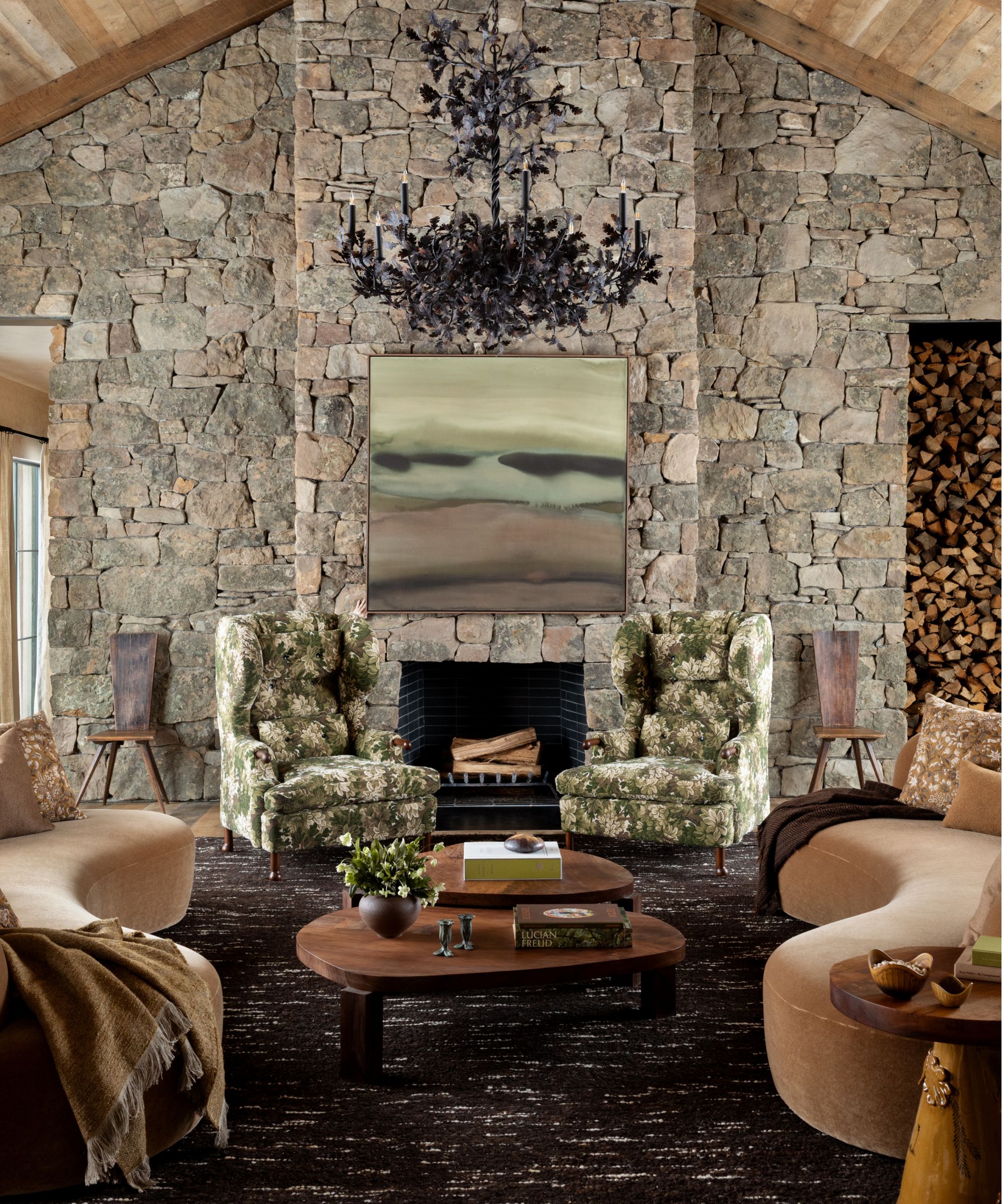 a large Great Room in Idaho with a wooden vaulted ceiling, stone clad walls, tall fireplace, black chandelier and curved velvet couches
