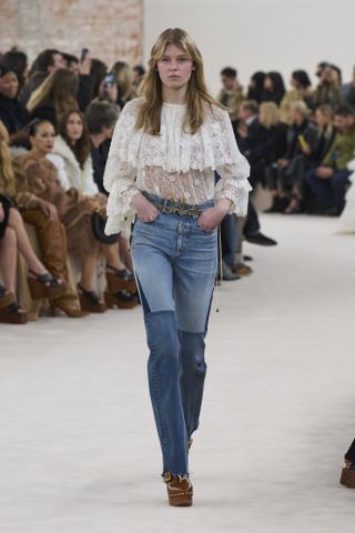 Chloe model wearing lace shirt, jeans, and brown clogs on fall/winter 2024 runway.