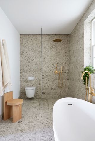 Bathroom with white tub, shower with clear glass doors and wooden chair.